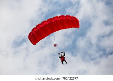 Parachuter descending with a red parachute against blue sky