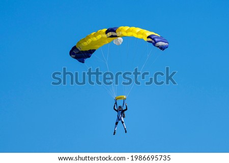 Parachutist with  yellow and blue parachute against a blue sky