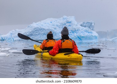Paradise Bay, Antarctica - 12 09 17: Candid rear view of a couple of kayakers Antarctic kayaking in snowfall, paddling a kayak in the icy sea with an Antarctica iceberg and glacier landscape