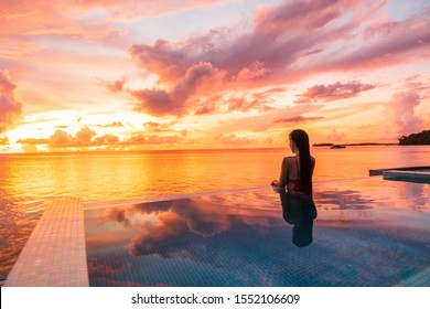 Paradise sunset idyllic vacation woman silhouette swimming in infinity pool looking at sky reflections over ocean dream. Perfect amazing travel destination in Bora Bora, Tahiti, French Polynesia.