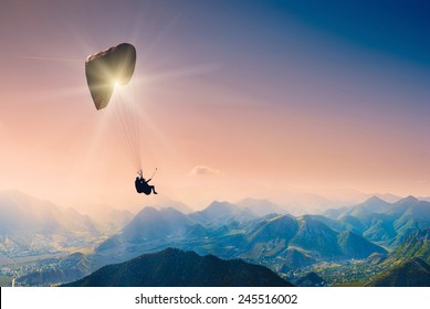 Paraglide silhouette over mountain peaks. 
