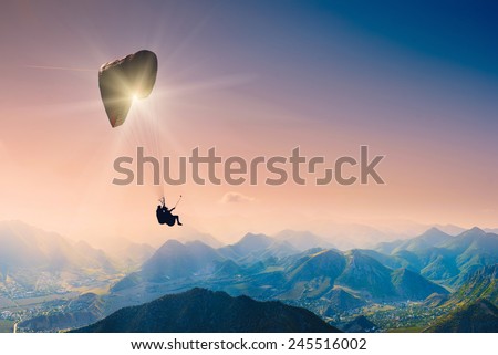 Paraglide silhouette over mountain peaks. 