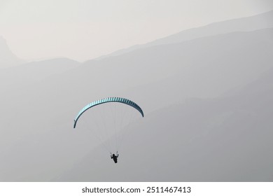 paraglider in the air with a colorful parachute in monochrome background of a hazy mountain range in different shades of grey - Powered by Shutterstock