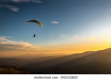paraglider flies over the mountains at sunset