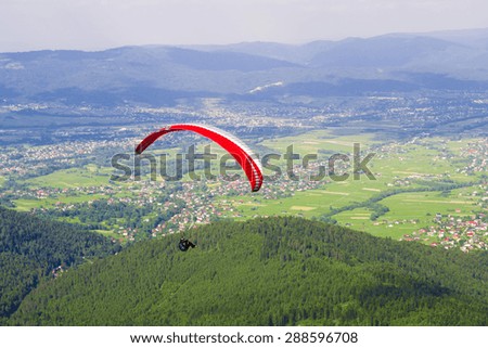 Paraglider flying over the fields on a sunny day.