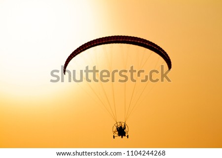 Paraglider flying with paramotor on dramatic sunset sky with big sun in orange and yellow. Concept for adventure extreme ultra light aviation 