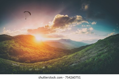 Paraglider silhouette in a light of sunset over the mountain valley. Instagram vintage stylisation.