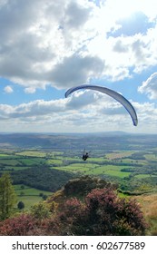 Paragliding down from the Wrekin in Shropshire with the paraglider in the foreground and rural Shropshire fields in the background with clouds above. 
