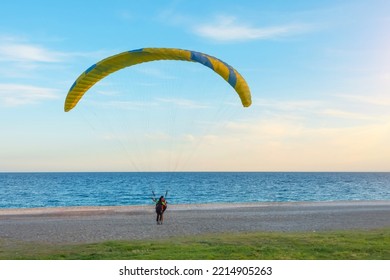 Paragliding, People Take Off From The Beach On The Ocean Coast During Sunset In The Evening