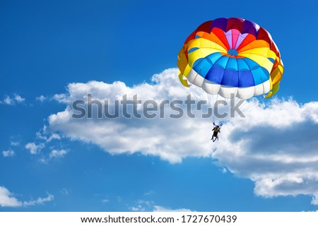 Paragliding using a parachute on the background of cloudy blue sky.