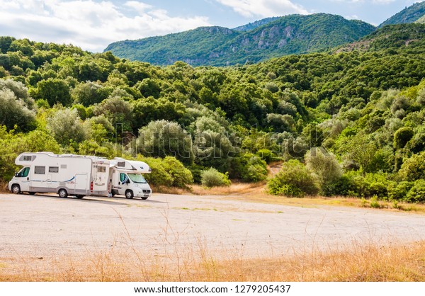 Paralia,\
Greece - June 12, 2013: Scenic view on two campers mobile homes\
parked on the parking lot under the high and green mountains range\
on the way from Thessaloniki to Athens in\
Greece