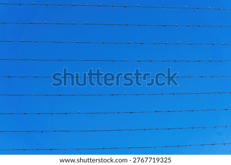 Parallel rows of decorative string lights wires stretched across clear blue sky forming minimal geometric pattern.