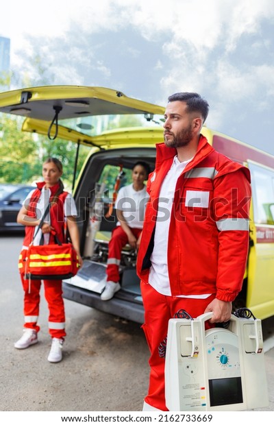 Paramedic nurse and emergency doctor at ambulance\
with kit. a paramedic, standing at the rear of an ambulance, by the\
open doors.