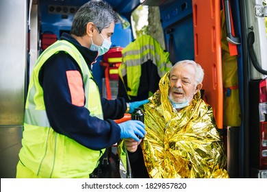 Paramedic rescues an elderly person in distress with an ambulance by covering him with a thermal blanket and making him drink a hot drink - Concept of first aid - Shutterstock ID 1829857820