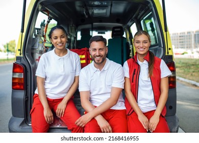 Paramedics and doctor standing at rear of ambulance. Doctor is carrying a medical trauma bag. Group of three paramedics standing in front of ambulance with smile.