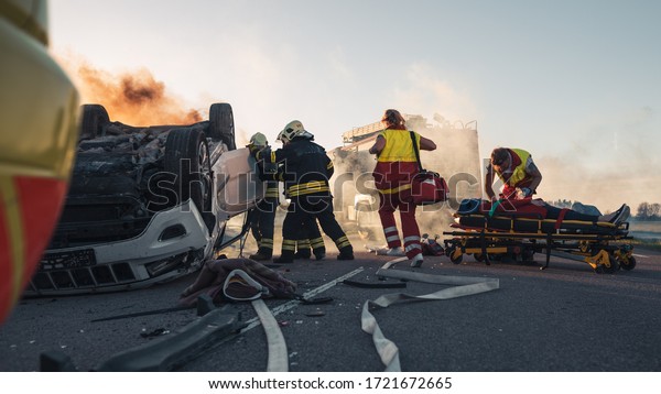 Paramedics and Firefighters Arrive On the Car Crash\
Traffic Accident Scene. Professionals Rescue Injured Victim Trapped\
in Rollover Vehicle by Extricating Them, giving First Aid and\
Extinguishing Fire