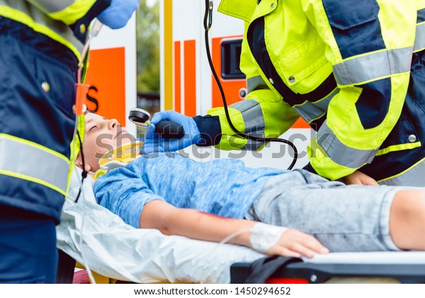 Paramedics measuring blood pressure of injured\
boy in front of\
ambulance