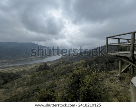 A paramo river viewed from a wooden balcony, framed by lush vegetation and a gray, cloud-covered sky. This photo captures the tranquil beauty of high-altitude waterscape and scenic paramo surroundings