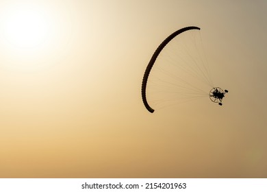 Paramotor vehicle tilted flying in a yellow sky by the sun. Concept of powered parachute or powered paraglider.