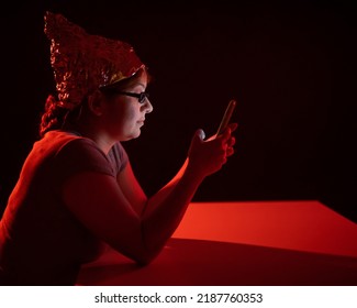 Paranoid Caucasian Woman Using Smartphone Wearing Tinfoil Hat. Conspiracy Theory. 