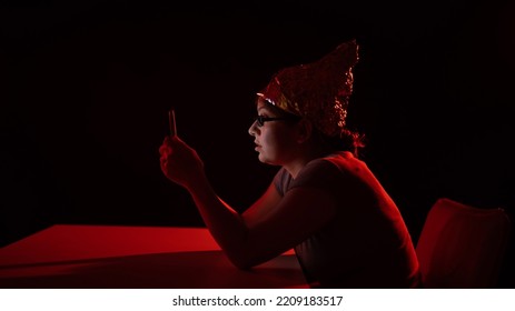 Paranoid Caucasian Woman Using Smartphone Wearing Tinfoil Hat. Conspiracy Theory. 