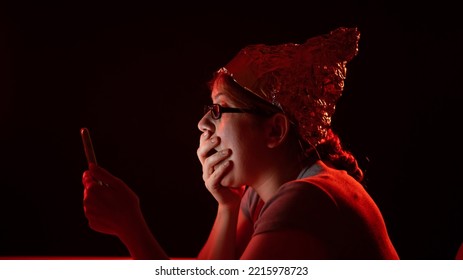 Paranoid Caucasian Woman Using Smartphone Wearing Tinfoil Hat. Conspiracy Theory. 