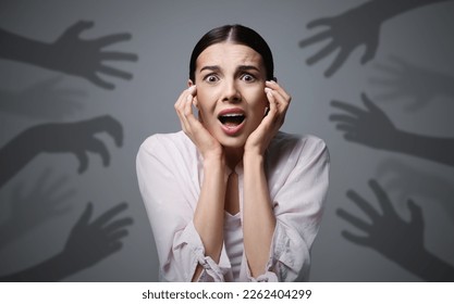 Paranoid delusion. Scared woman screaming on grey background. Shadows of hands reaching for her symbolizing fear and anxiety