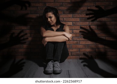 Paranoid individual. Scared woman sitting near brick wall and having delusion as hands reaching for her