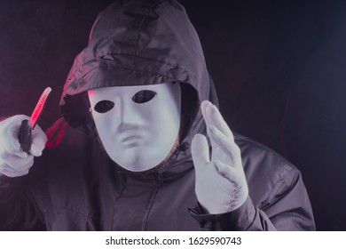 Paranormal,horror,scary concept,a man wearing a hooded jacket,he has a mask and gloves on,he is holding a knife,he is standing in a treating manner,there is a dark background. - Powered by Shutterstock