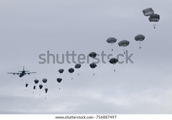 Paratroopers jump from C-130 Hercules military\
plane on evening