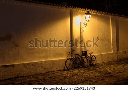 Paraty, Brazil. Bicycles on the wall under the light of old street lamps at night. Street made with stones from the colonial period.