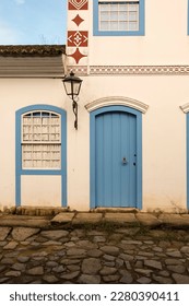 Paraty, Brazil. Facade of a colonial house from 1836 in white and blue colors. Door, window and old street lamp. Background blue sky.