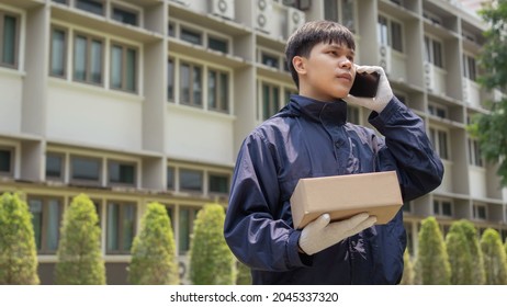 Parcel Delivery Concept The Mail Carrier Standing In Front Of The Building And Calling His Customer To Confirm The Right Address For Distributing The Parcel Post.