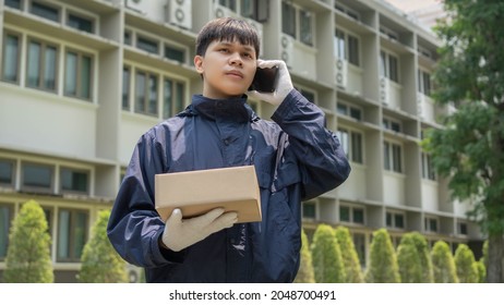 Parcel Delivery Concept The Mail Carrier Standing In Front Of The Building And Calling His Customer To Confirm The Right Address For Distributing The Parcel Post.