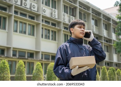 Parcel Delivery Concept The Mail Carrier Standing In Front Of The Building And Calling His Customer To Confirm The Right Address For Distributing The Parcel Post.