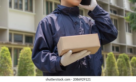 Parcel Delivery Concept The Mail Carrier Standing In Front Of The Building And Calling His Customer To Confirm The Right Address For Distributing The Parcel Post.