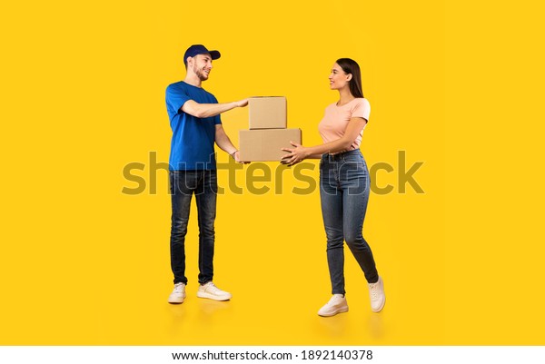 Parcel Delivery. Woman Receiving Boxes From Male\
Courier Standing Over Yellow Studio Background. Post Package\
Delivering And Transportation, Couriers Service Concept. Full\
Length