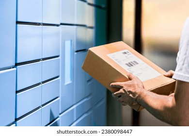 Parcel locker and package delivery service machine. Collect packet at mail storage station at post office. Man holding a box in hand. Blue shipment terminal automat pick up. Courier or customer.