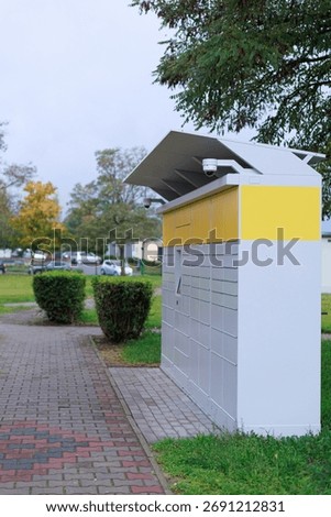 Parcel locker surrounded by grass and trees in urban park. Concept of sustainable logistics and green city solutions.