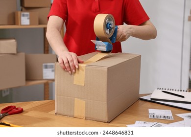 Parcel packing. Post office worker taping box at wooden table indoors, closeup