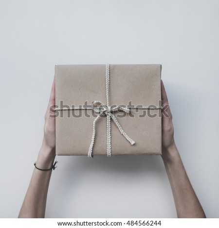 Parcel wrapped in kraft paper, in female hands on a white background. Minimalistic photo. Womans hand holding gift box. Top view.
