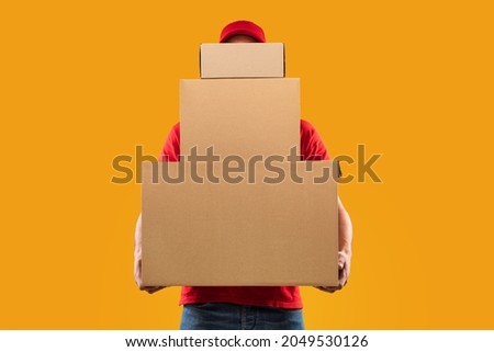 Parcels Delivery. Unrecognizable Courier Guy Holding Many Big Cardboard Boxes Delivering Packages To You Posing Standing In Studio Over Yellow Background. Postal Shipping Service Concept