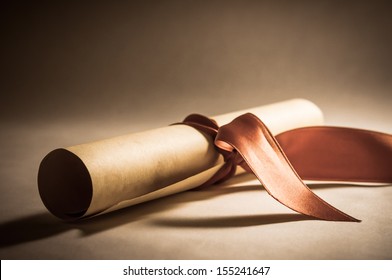 A parchment diploma scroll, rolled up with red ribbon laid at an oblique angle.  Processed to give a vintage or retro appearance. - Shutterstock ID 155241647