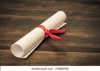 A Parchment Diploma Scroll, Rolled Up With Red Ribbon On Wooden Backgroung