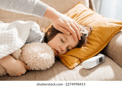 A parent checks the temperature of a sleeping child with his hand. The sick boy sleeps on the couch in the living room. Sick children - Powered by Shutterstock