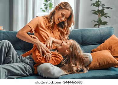 Parent and child connection. Excited blond girl laying on mother's lap and looking at mom while laughing. Delighted mother tickling daughter and smiling while enjoying spending time together at home. - Powered by Shutterstock