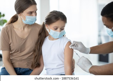 Parent And Child In Face Masks Getting Vaccinated Against Coronavirus, Doctor Making Injection Of Covid-19 Vaccine At Clinic. Mother And Daughter Participating In Immunization Campaign