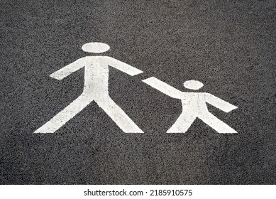 Parent Child Pedestrian Road Sign, White Paint On Tarmac, Indicating A Safe Place For Families To Cross A Carpark Road Towards A Busy Shopping Centre. 