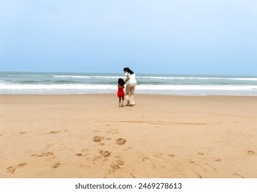 A parent and child share a peaceful moment on the sandy shore, waves gently lapping at their feet. The overcast sky adds to the calmness of this family scene - Powered by Shutterstock