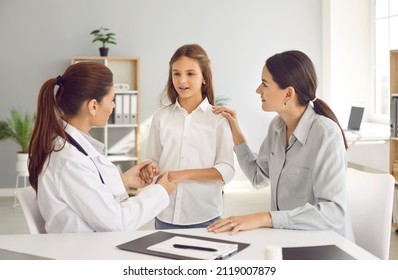 Parent And Child Talking To Family Doctor. General Practitioner Holding Kid By Hands During Interview. Pediatrician Listening To Little Girl Who Came To Hospital With Her Mother. Trust Concept